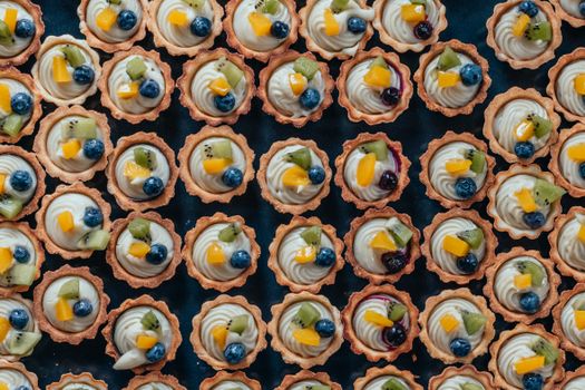 Plateau de mini-tartes garnies de crème et de fruits colorés, idéal pour un buffet ou un dessert festif.