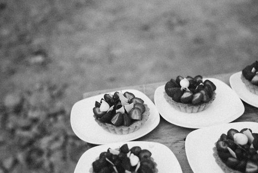 Assiette de tartelettes aux fruits, décorées de fraises et myrtilles, sur une table en bois.