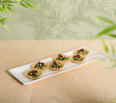 Bouchées thaï au crabe présentées sur un plat blanc, décorées de légumes et herbes fraîches.