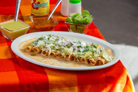 Assiette de taquitos au poulet et pommes de terre, garnis de chou, oignons et coriandre, sur nappe à carreaux colorée.